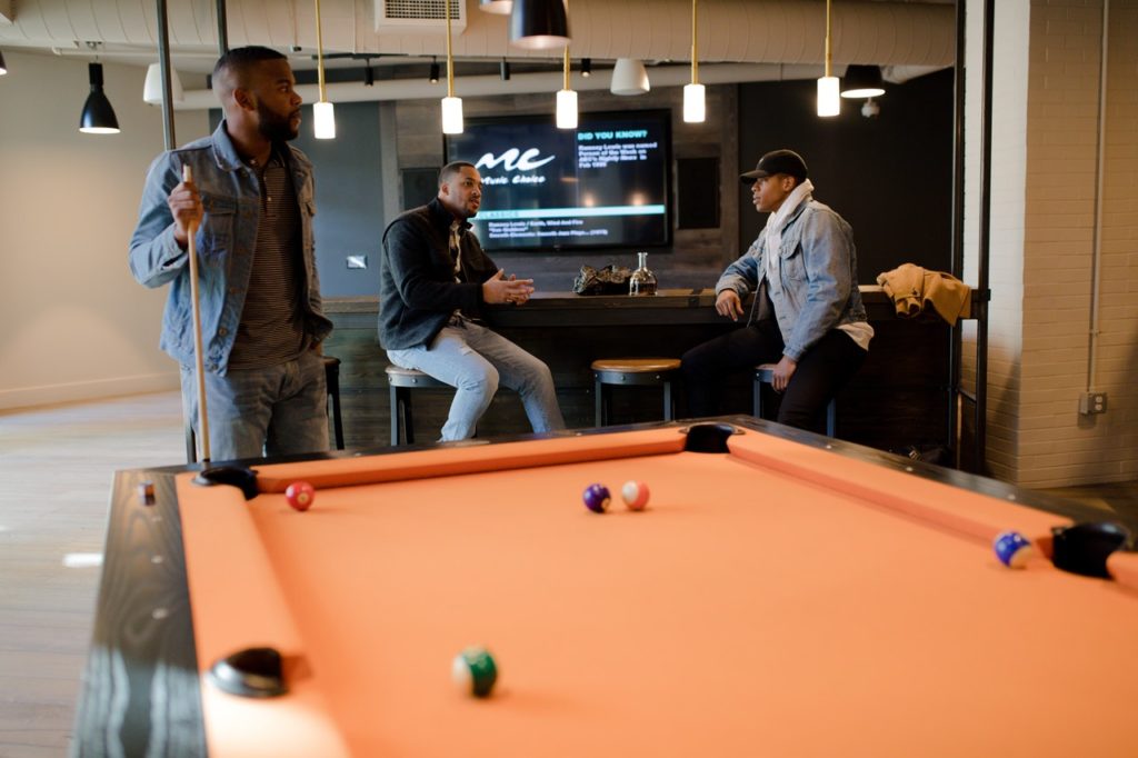 Billiards Table, With Three Men Sitting Around Near a Bar